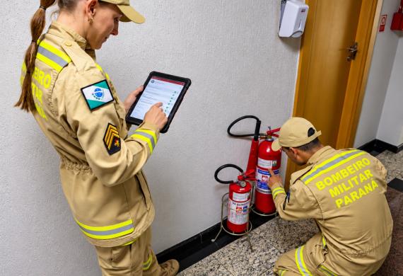 Dois bombeiros verificando extintores e fazendo anotações em um tablet